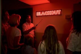 Auf dem Weg zur Blackoutstation Tourguide und Besuchergruppe vor dem roten LED-Schild „Blackout“ auf dem Weg zur Blackoutstation im Donaukraftwerk Ybbs-Persenbeug.